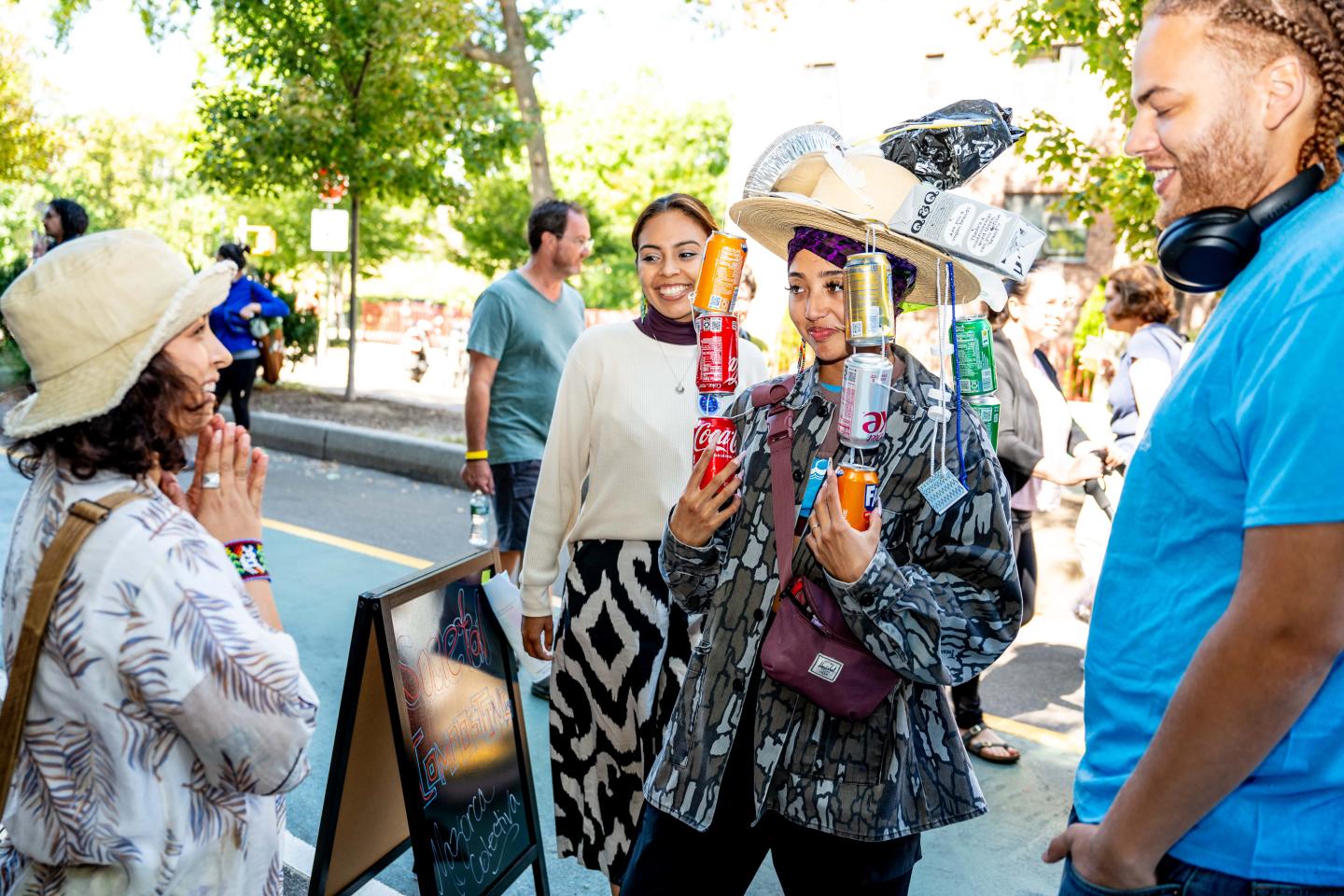 A woman wearing recycled items as a hat, including soda cans hanging down at a street fair during New York City Climate Week