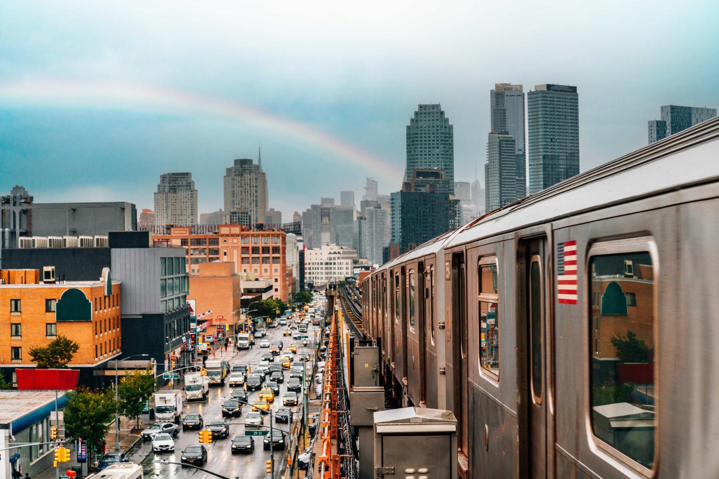 A subway approaches New York City with a rainbow in the distance