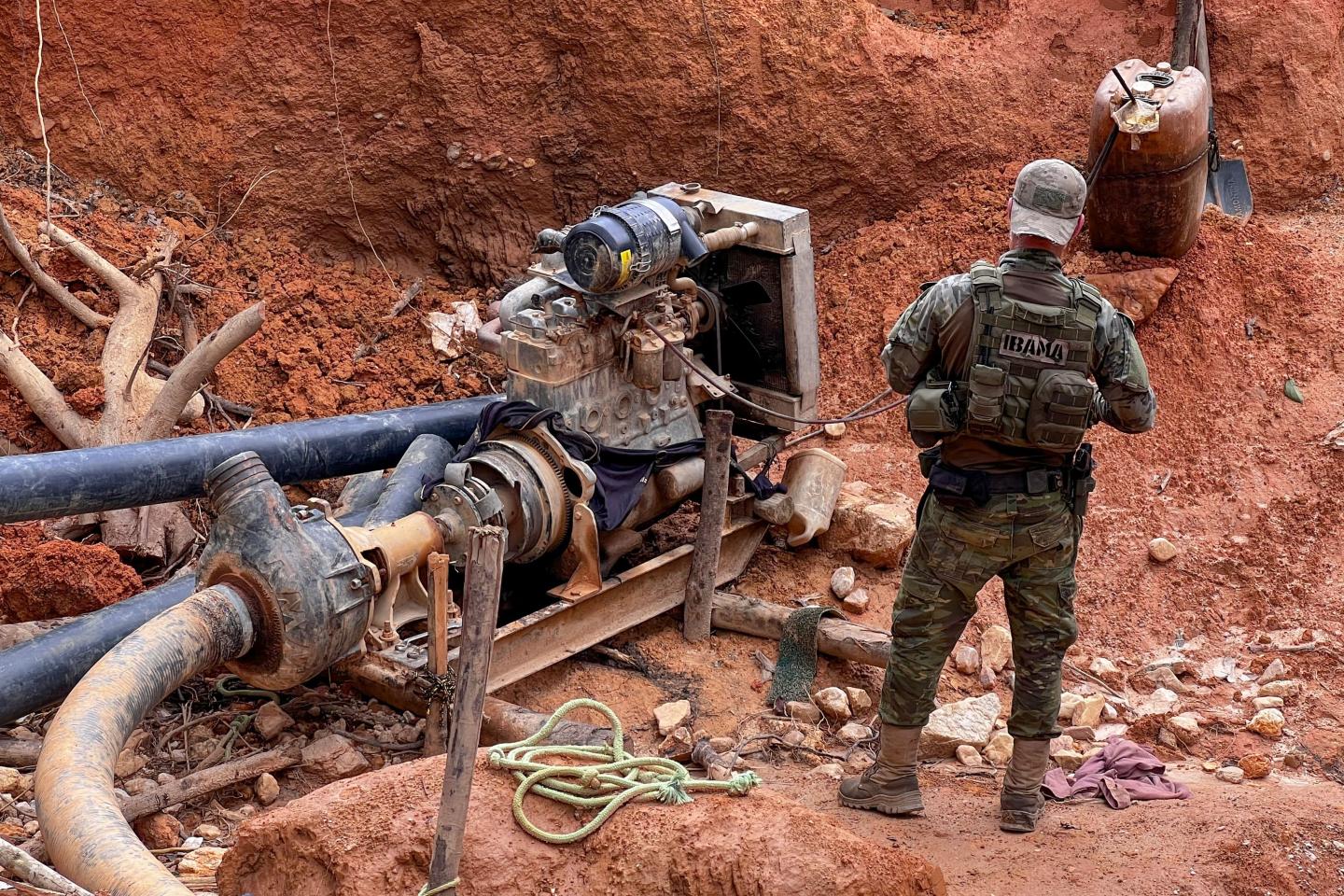 An armed man with IBAMA on a patch on his bank standing in an illegal gold mine