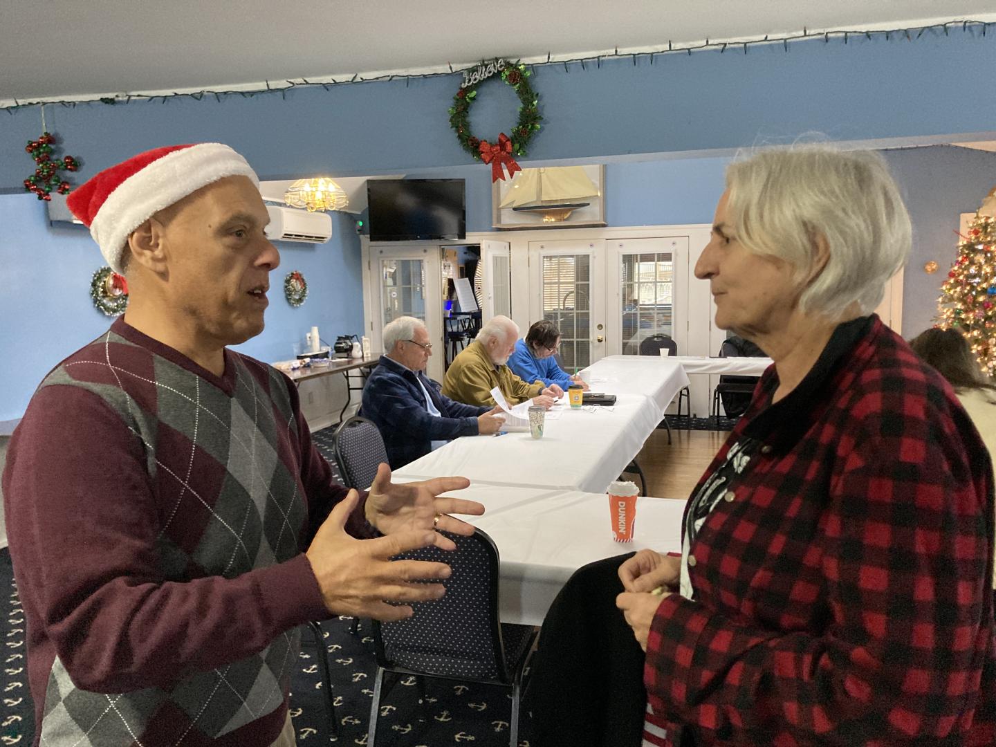 Joseph DeStefano in a Santa hat chatting with Maura Spery in a meeting hall