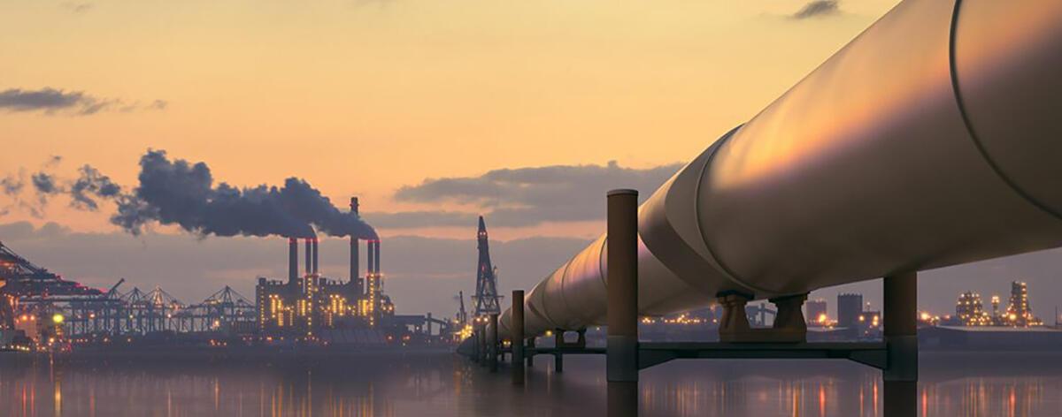 A refinery in the distance with a pipeline in the foreground 