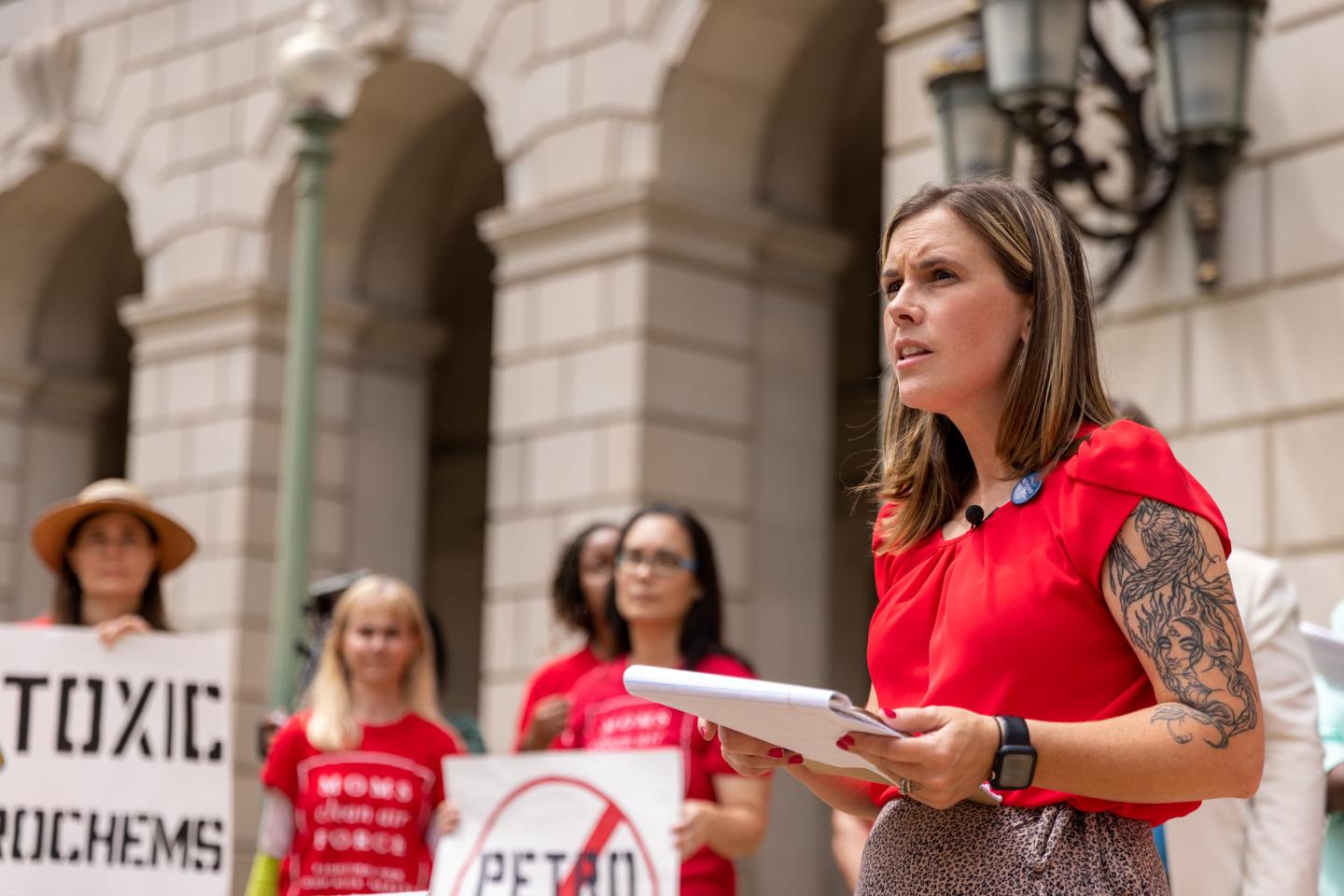 Jess Conard speaking in front of people holding signs in protest against toxic chemicals