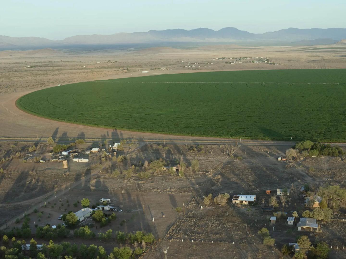 An aerial shot of a large semi-circle of green, lush land surrounded by homes without dirt yards and no water