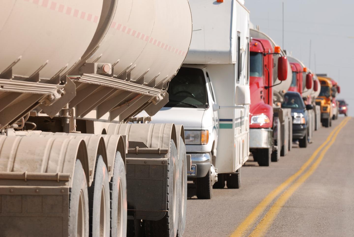 A row of trucks and other large vehicles driving down the road