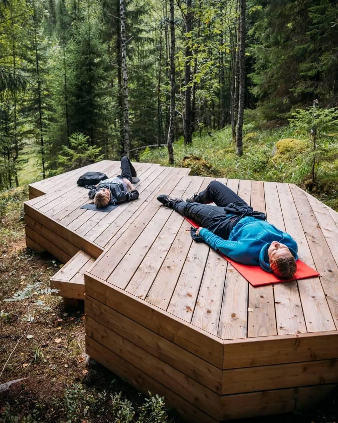 Two people laying on wooden platforms in a forest