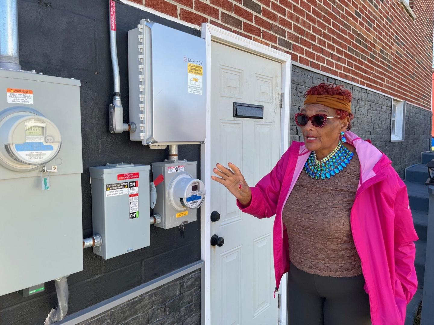 Mary West standing outside of her house pointing to the electric meter
