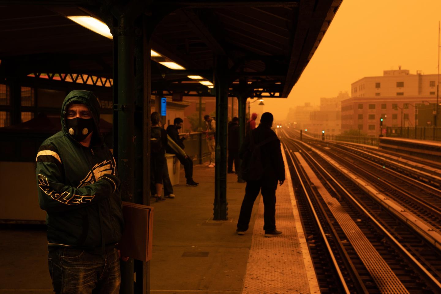 A group of people on a subway platform wearing masks because the air is orange and hazy from wildfire smoke