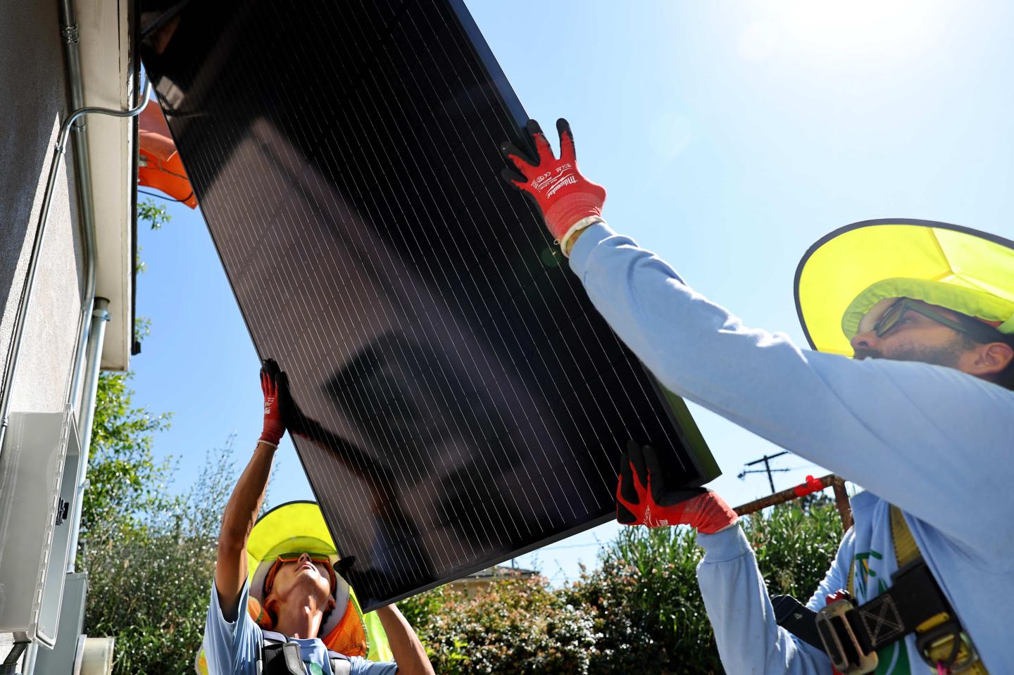 Two people lifting a solar panel onto a roof
