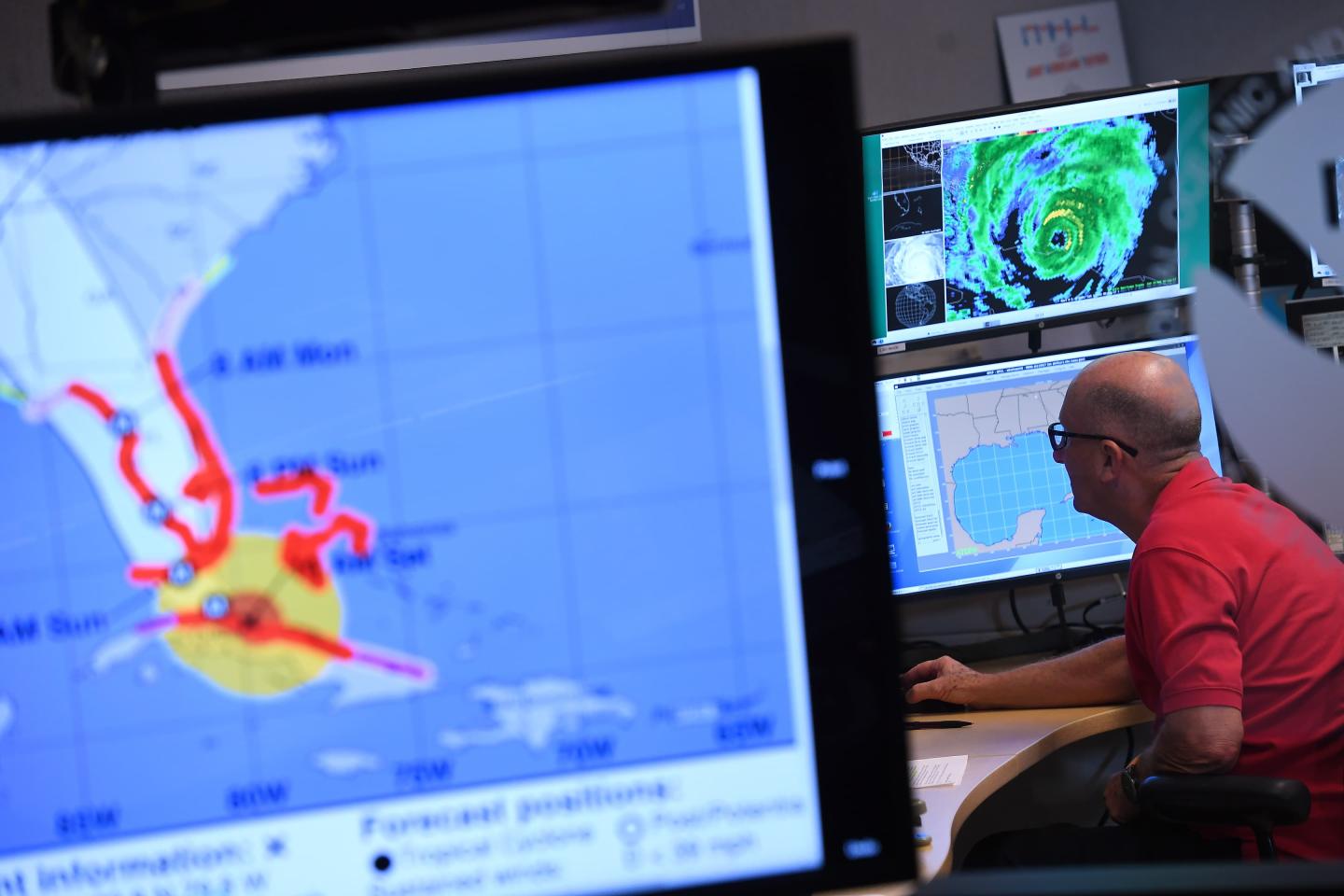 A man in the background working at a computer with weather information in the foreground