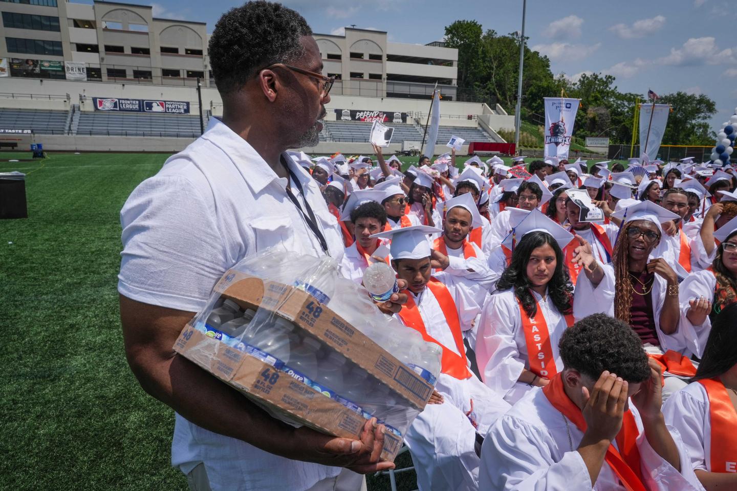 A man handing out bottles of water to high schoolers at their graduation 
