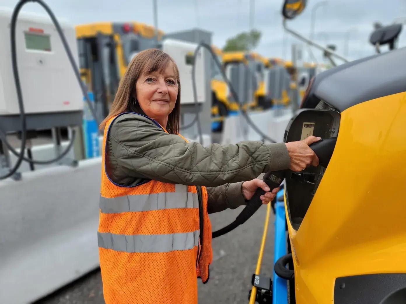 A person in an orange vest plugging in an electric school bus