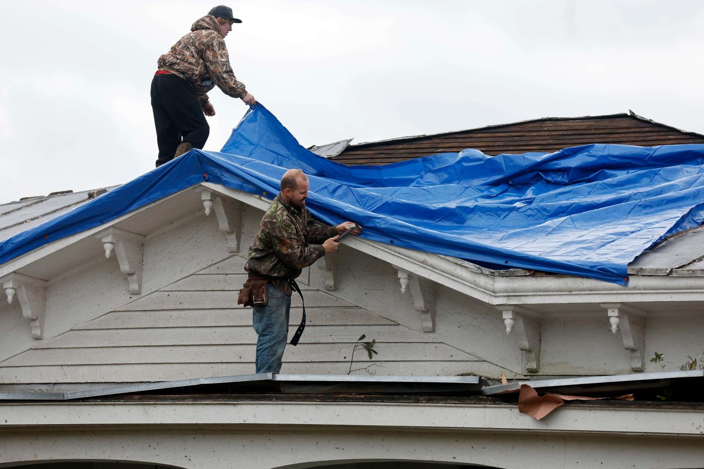 Two people putting a blue tarp on a roof