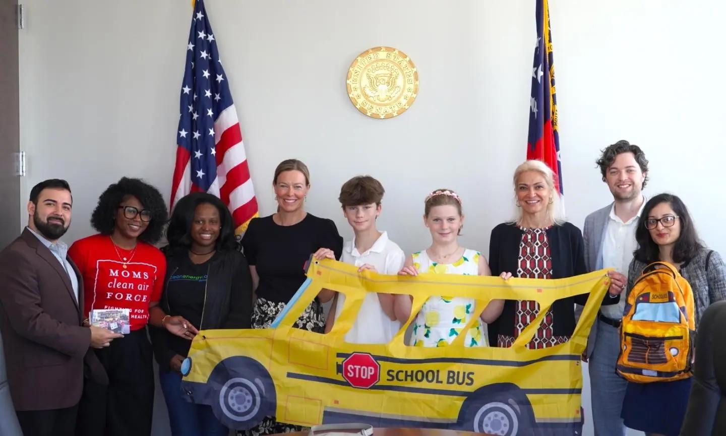 A group of people holding a yellow school bus poster