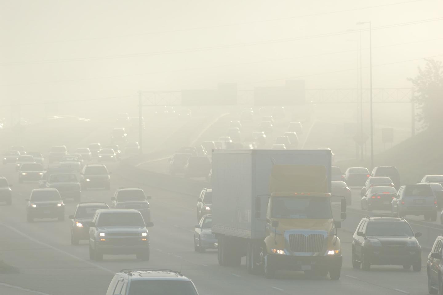 An incredibly hazy and smoggy picture of cars and trucks driving down the highway