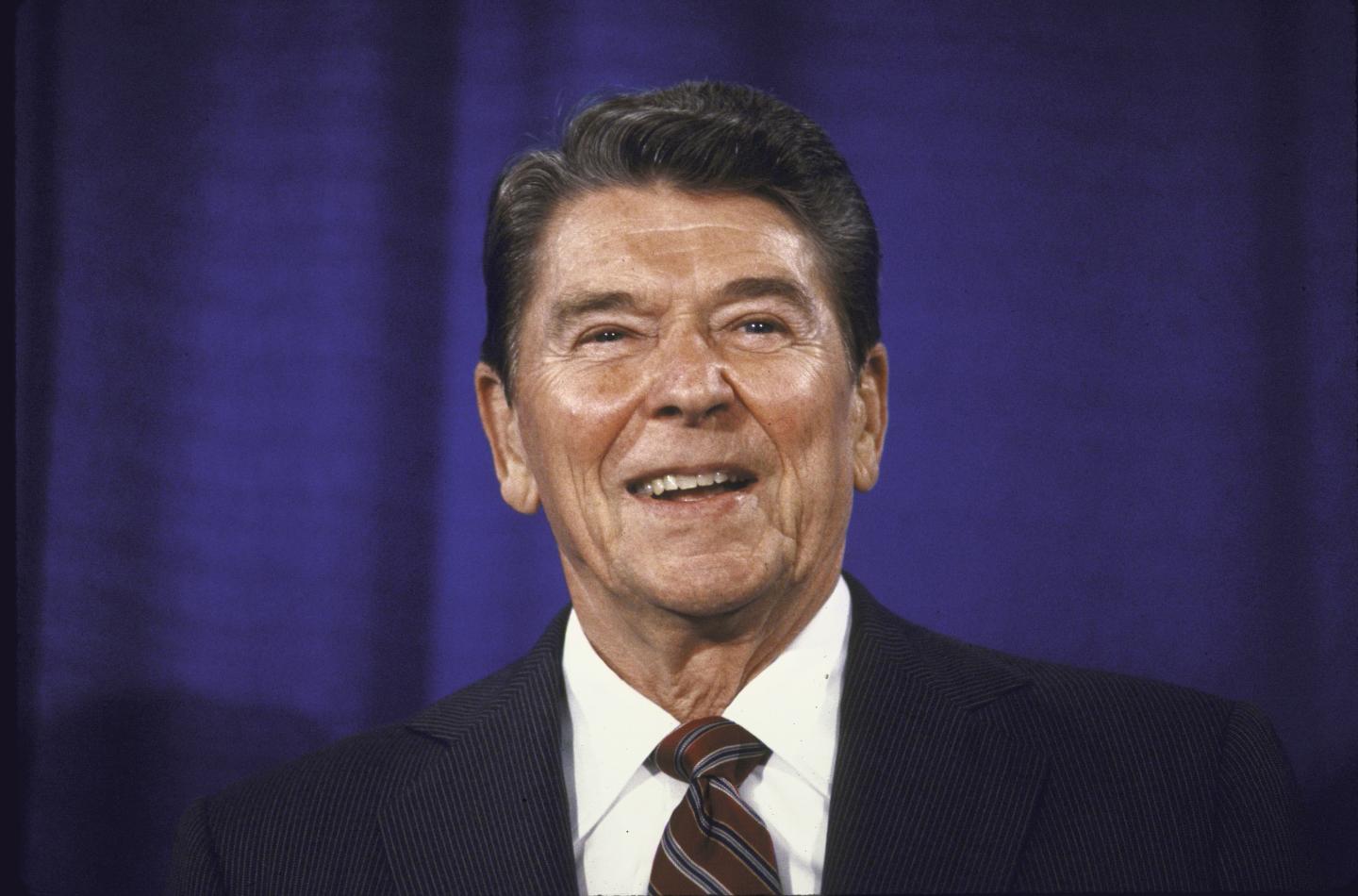 Ronald Reagan smiling in front of a blue curtain