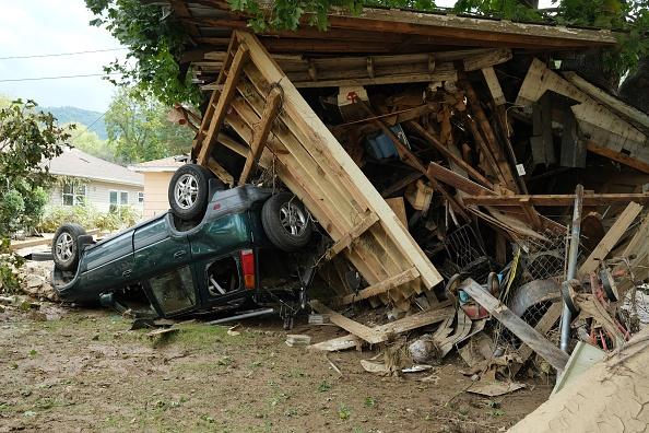 A car flipped over next to a broken down shed