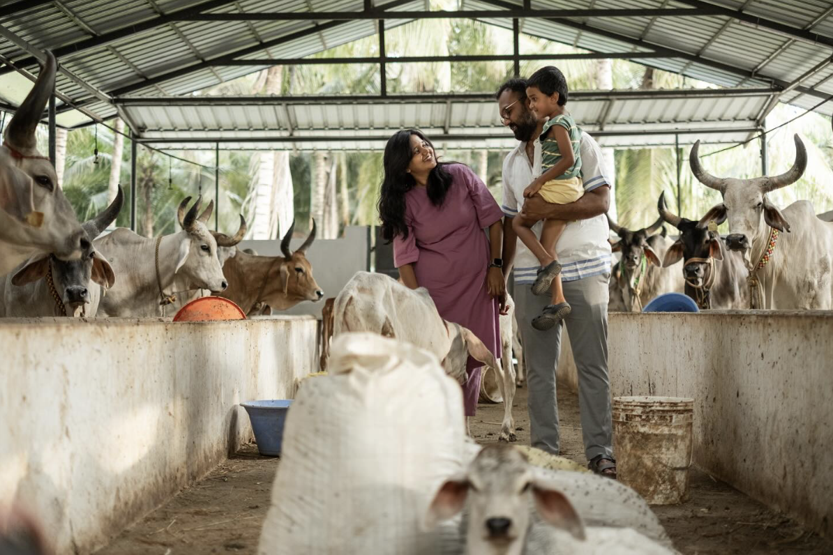 K.S.M. Dinesh holding his child and standing next to his wife inside his dairy farm