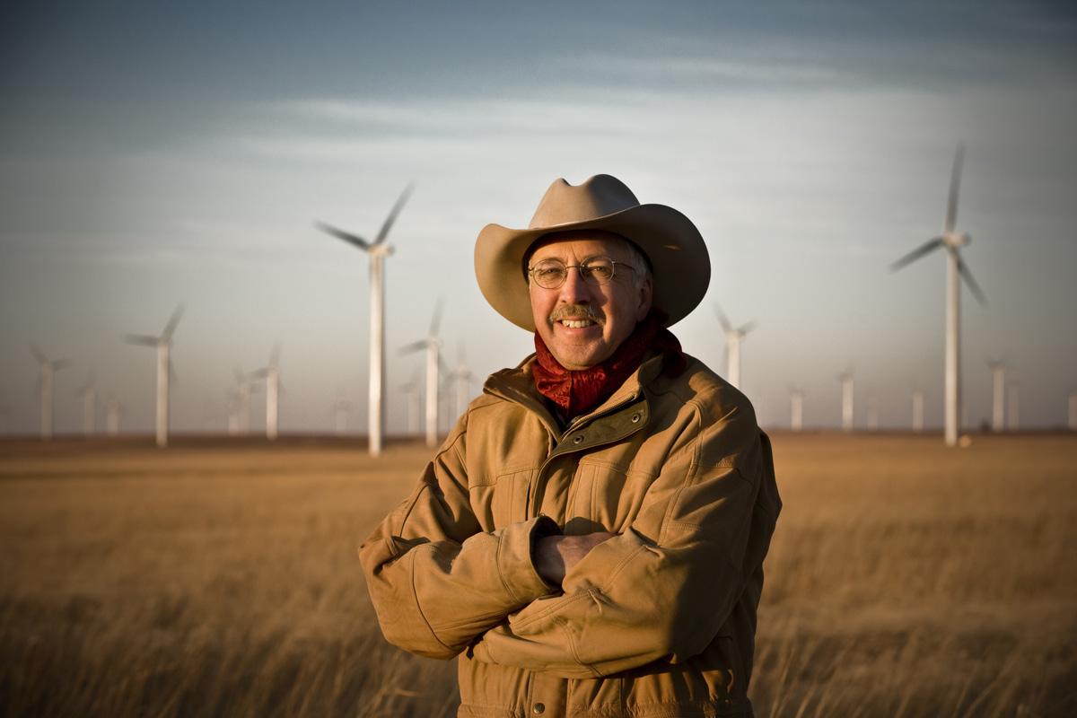 Pete Ferrell standing in a grass field in front of wind turbines