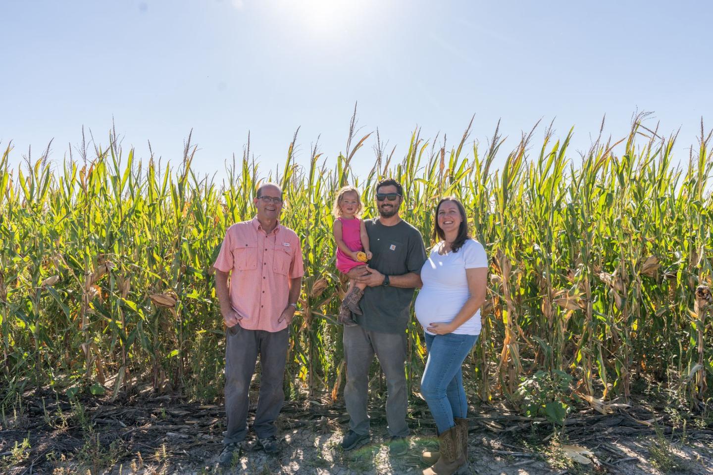 Dwane Roth next to his nephew Zion who is alongside his family. They're standing in front of a corn crop field