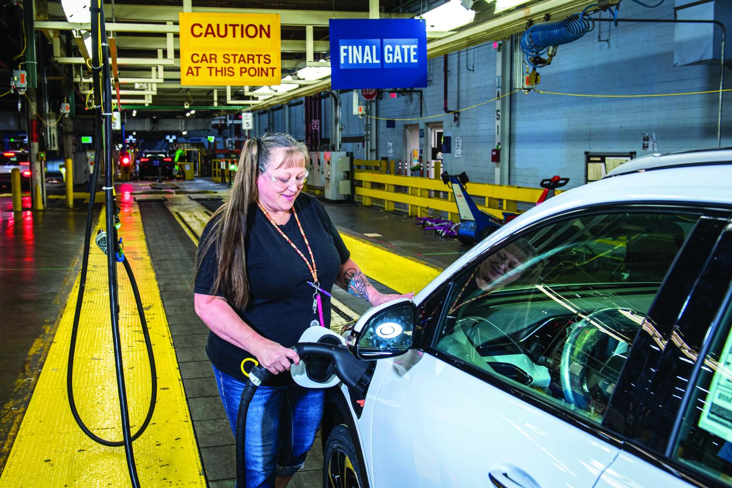 A woman manufacturing worker inserting charging cable into an EV vehicle