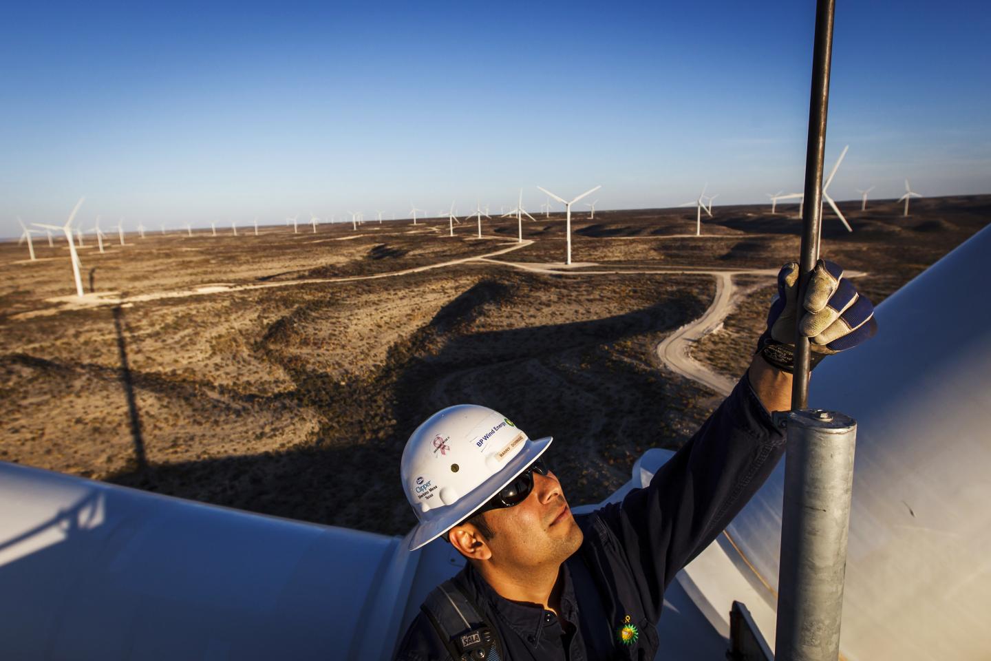A person wearing a safety helmet and gloves working on top of a wind turbine structure