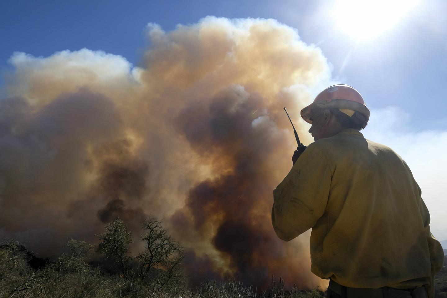A person talking into a walkie talkie while standing in front of wildfire smoke
