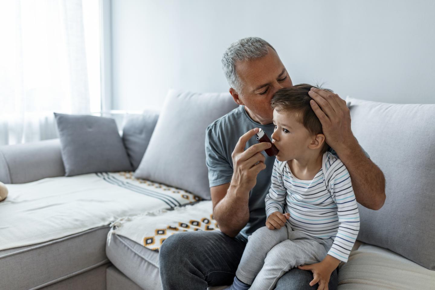 A man holding up an inhaler to a child as they sit on his lap