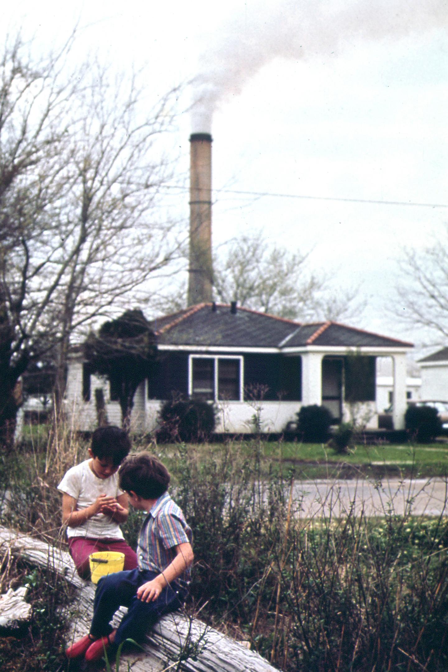 Two children sitting in front of a gas pipe that's blowing out smoke