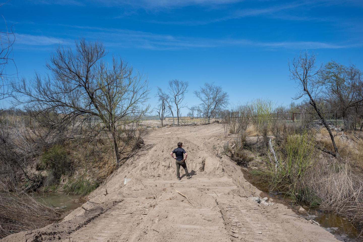 A man surveys water flow from a dusty road