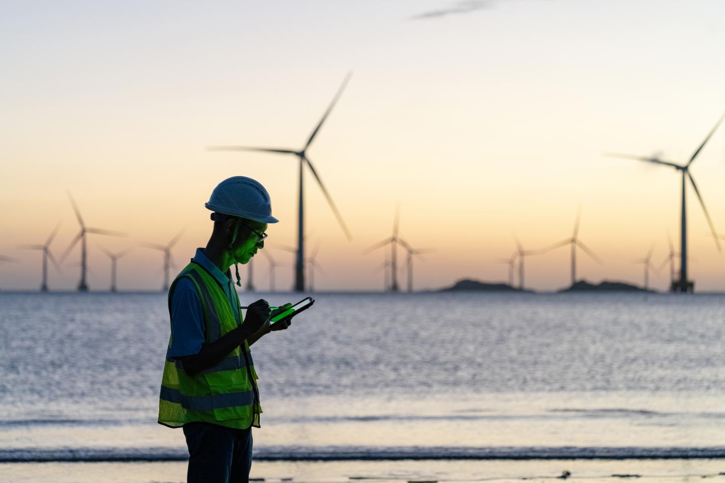 A worker looking at a device while standing in front of several wind turbines