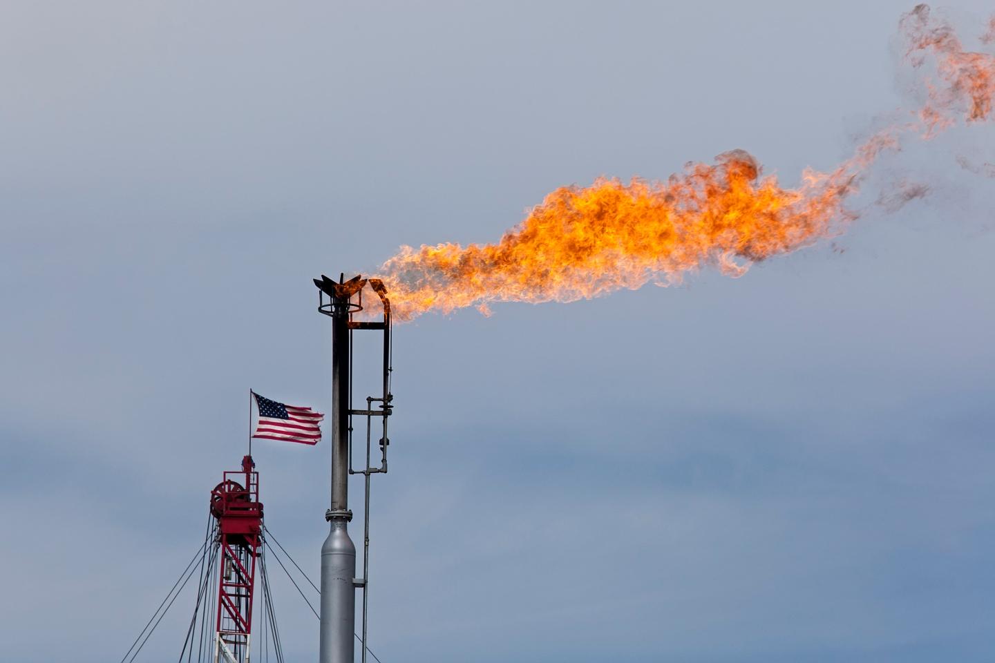 A blast of fire coming from a gas pipe with an American flag flying behind it