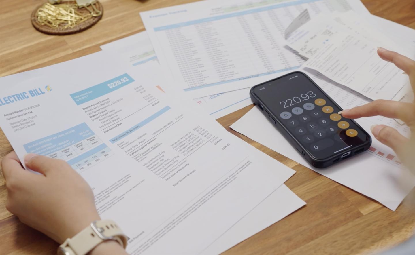 Someone going through their electric bill while using their calculator on their phone