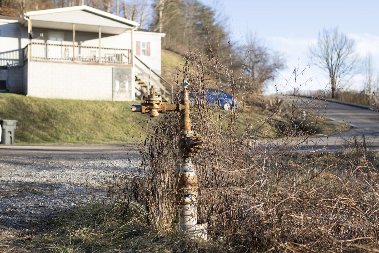 A rusty pipe sticking out of the ground with a house and car in the near background