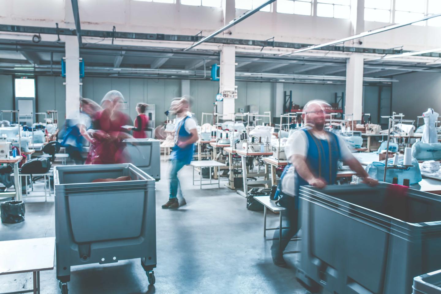 People moving quickly in a factory and that movement is causing their faces to blur