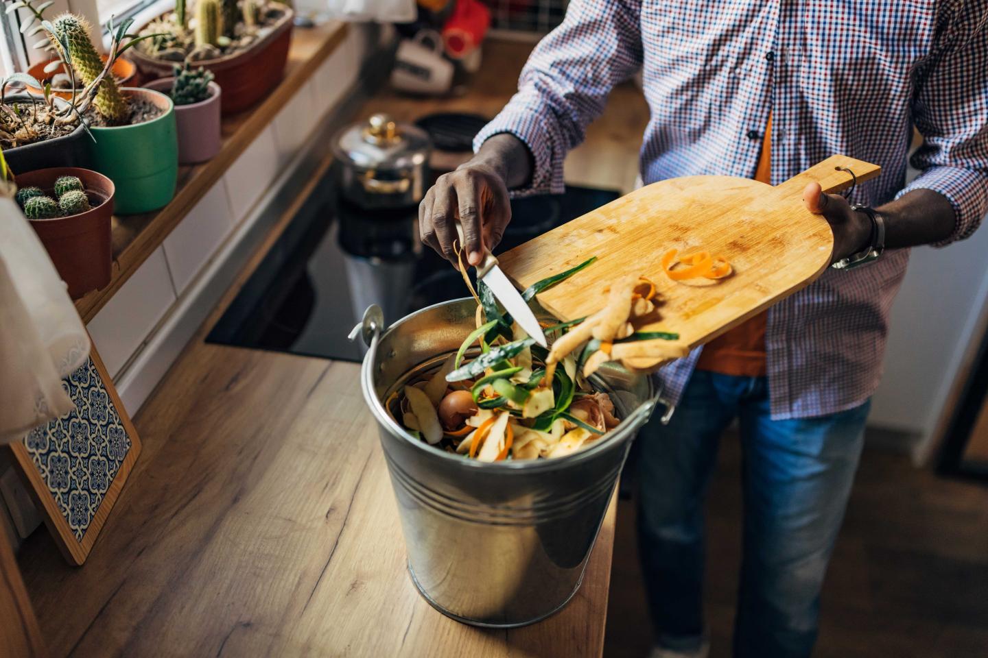 Someone scrapping scraps off a cutting board into a bin