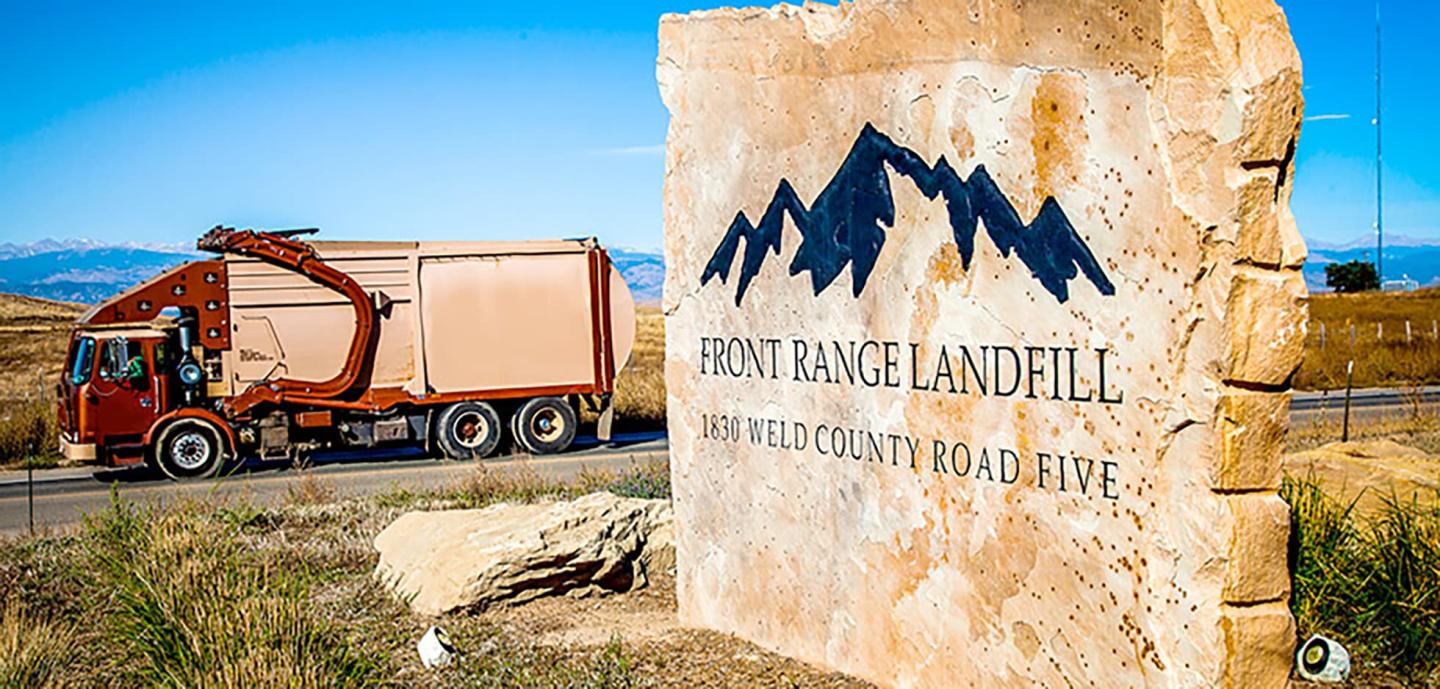 A trash truck driving by a sign for the Front Range Landfill in Erie, Colorado