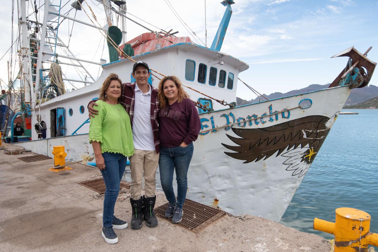 Irma Cervantes, her son and her business partner standing in front of a boat