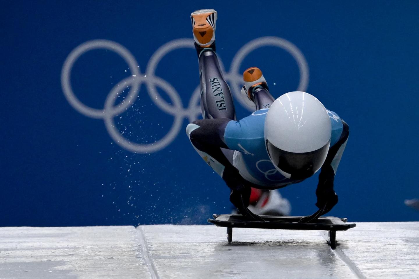 Katie Tannenbaum hopping onto a skeleton sled with the Olympics rings behind her