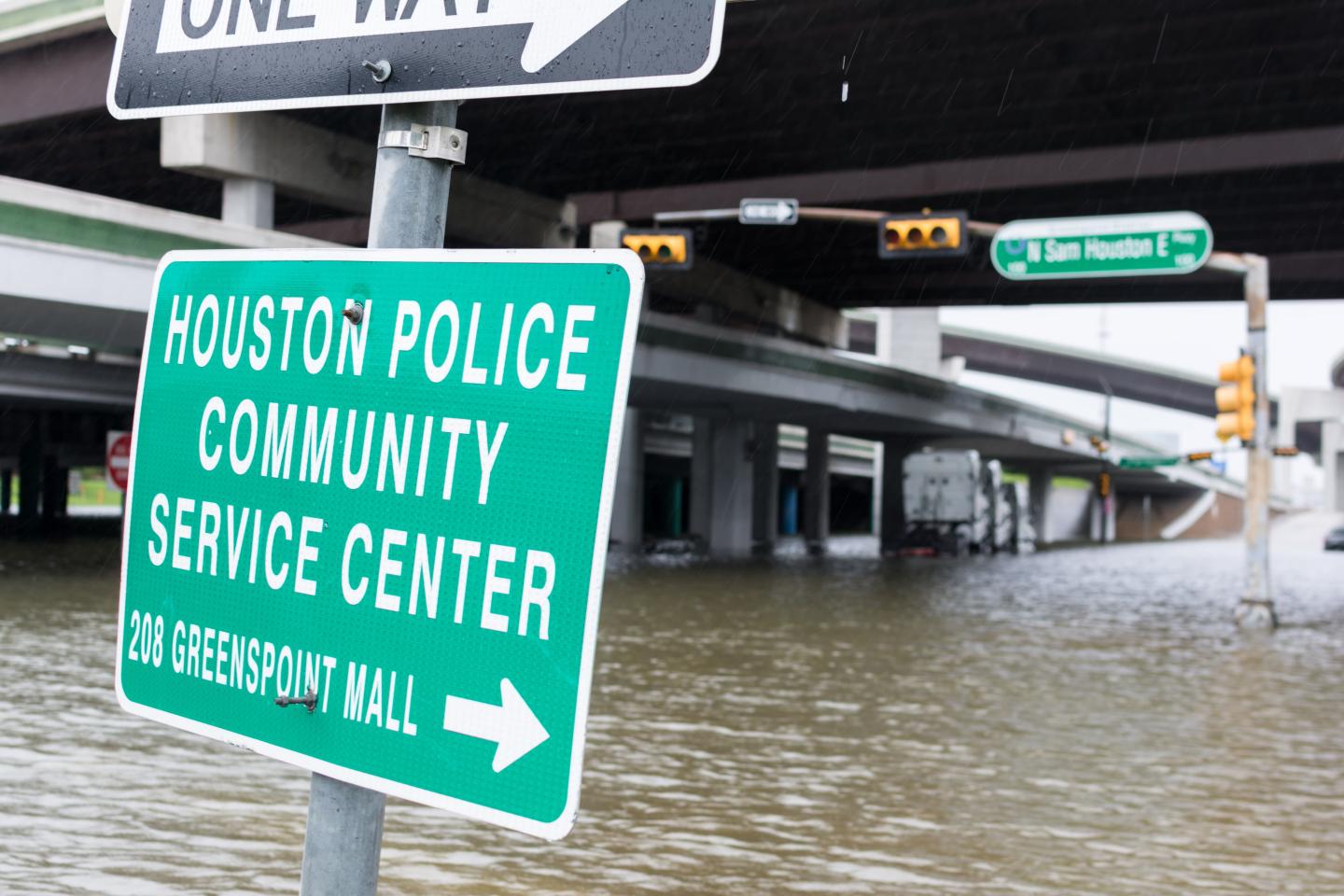 A flooded street with a sign for the Houston Police Community Service Center in the foreground 