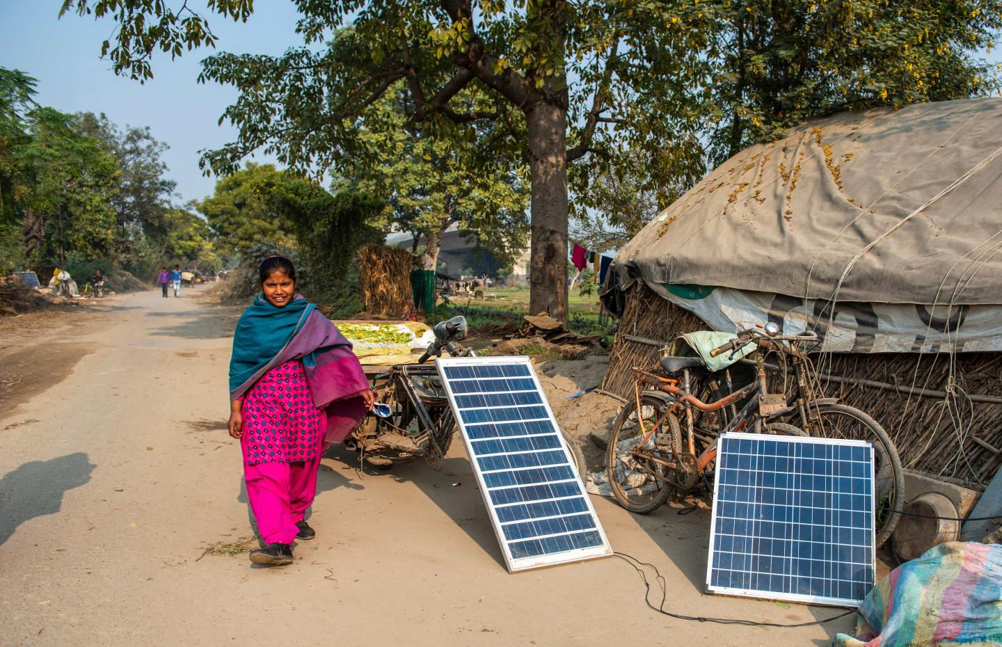 An Indian woman walking past two solar panels charging on the ground