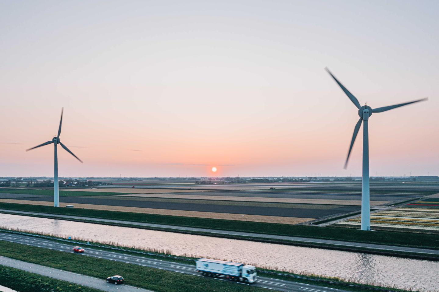 A truck driving on the foreground and large wind turbines in the background
