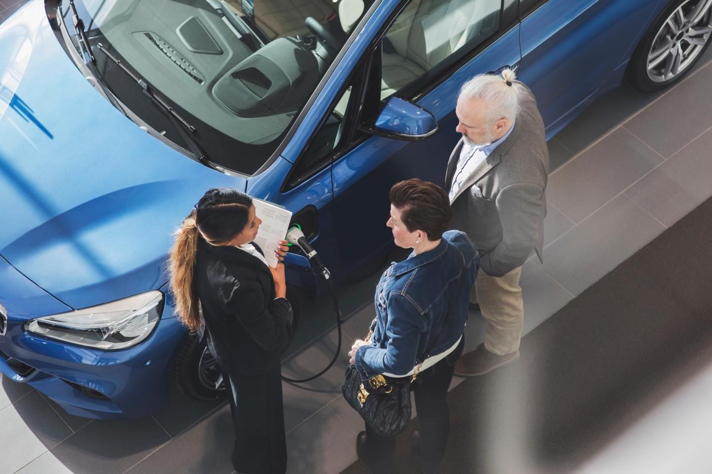 An overhead shot of three people standing near a car in a showroom