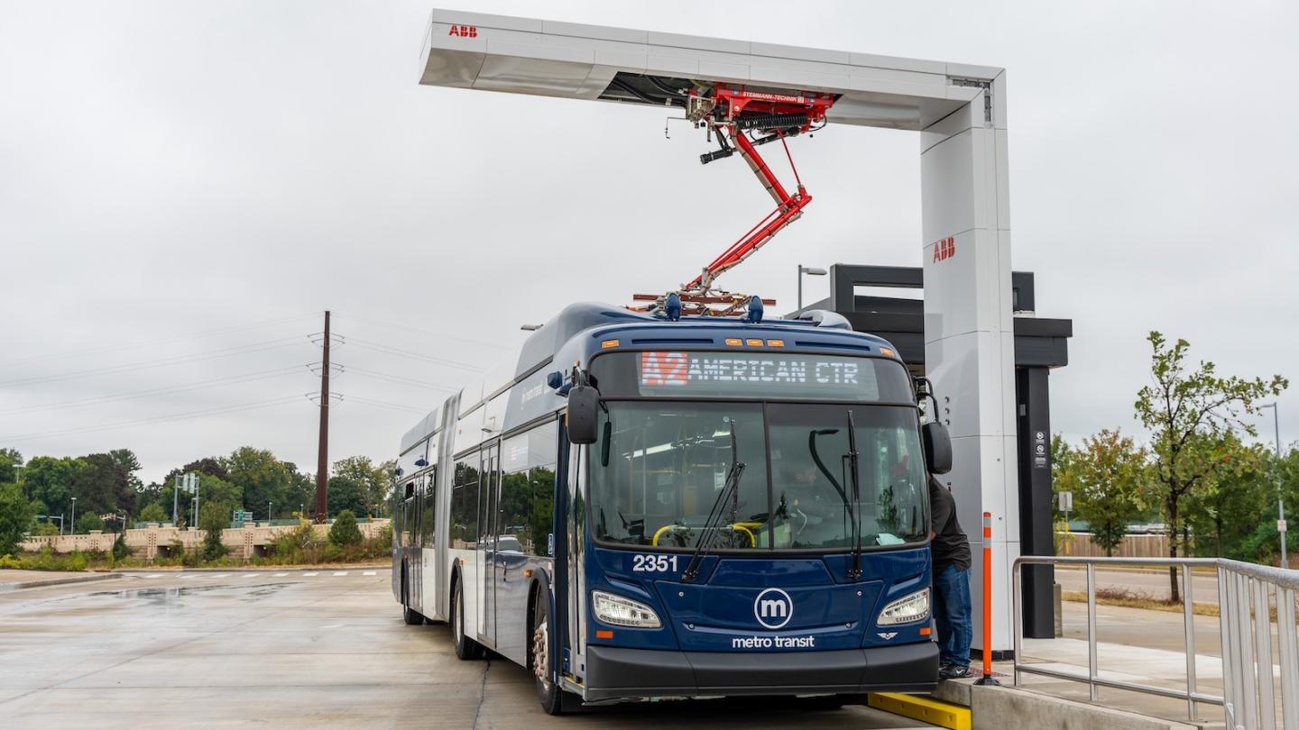 An electric bus stopped at a bust stop and charging with an overhead charger