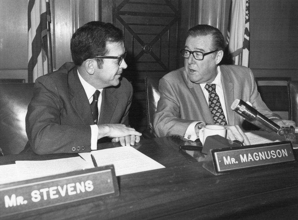Black and white photo of Senators Ted Stevens and Warren Magnuson sitting next to each other with nameplates in front of them