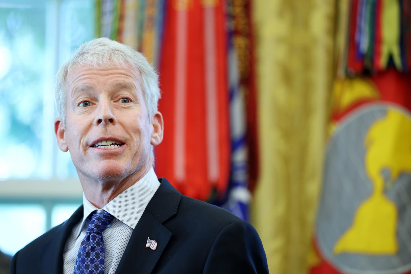 Chris Wright in front of flags and gold curtains