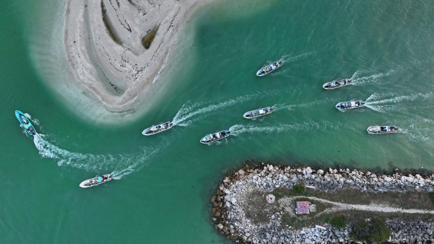 Boats driving on a blue waterway between two rocky piers