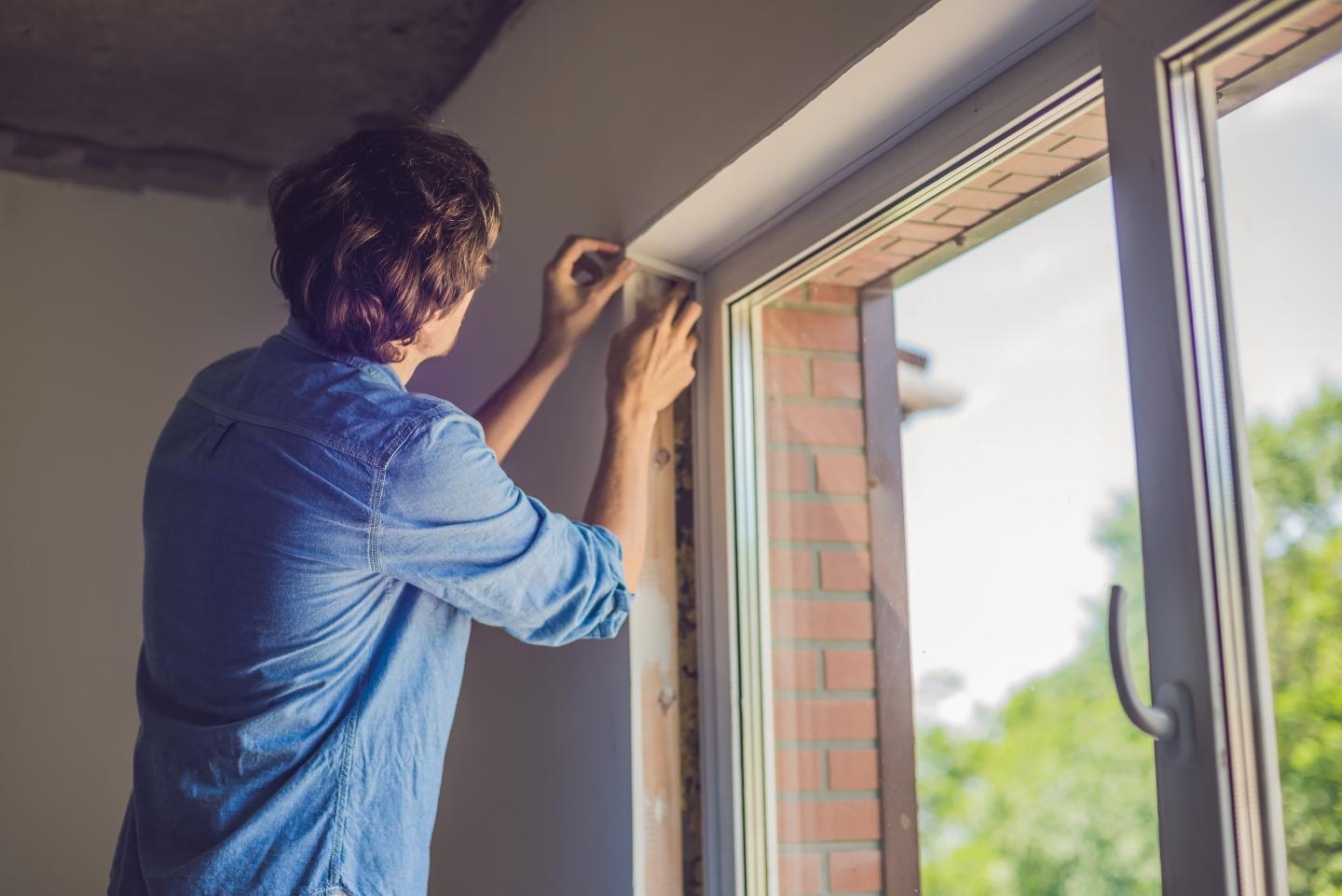 A person putting weather stripping onto windows