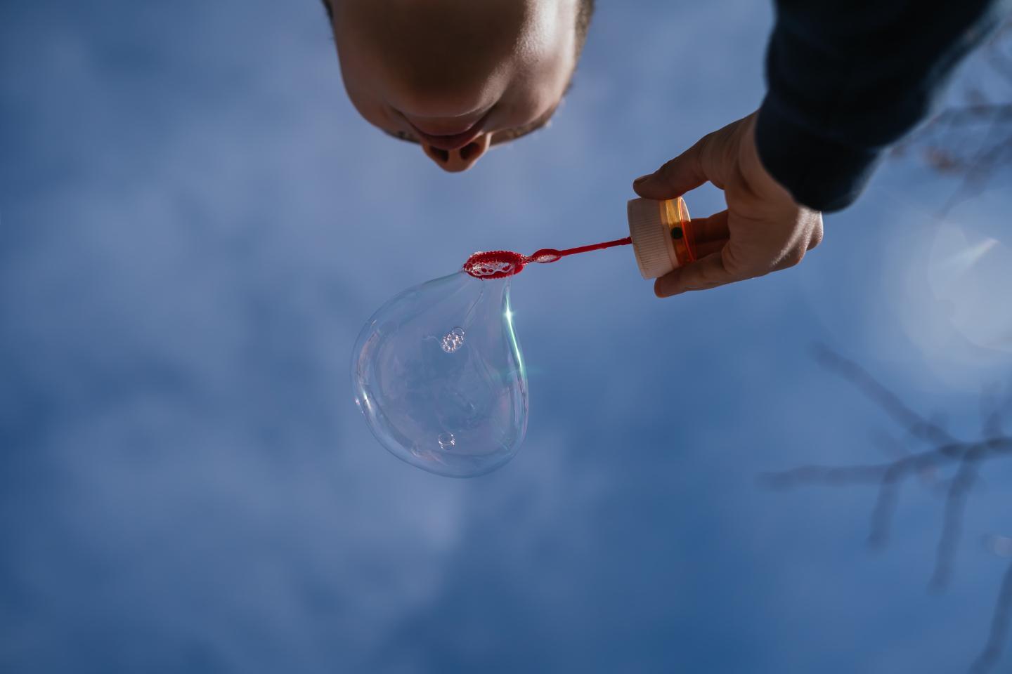 A child blowing a bubble with a blue sky above