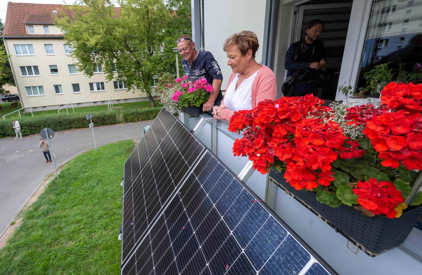 Two people looking over their balcony that has red flowers and solar panels