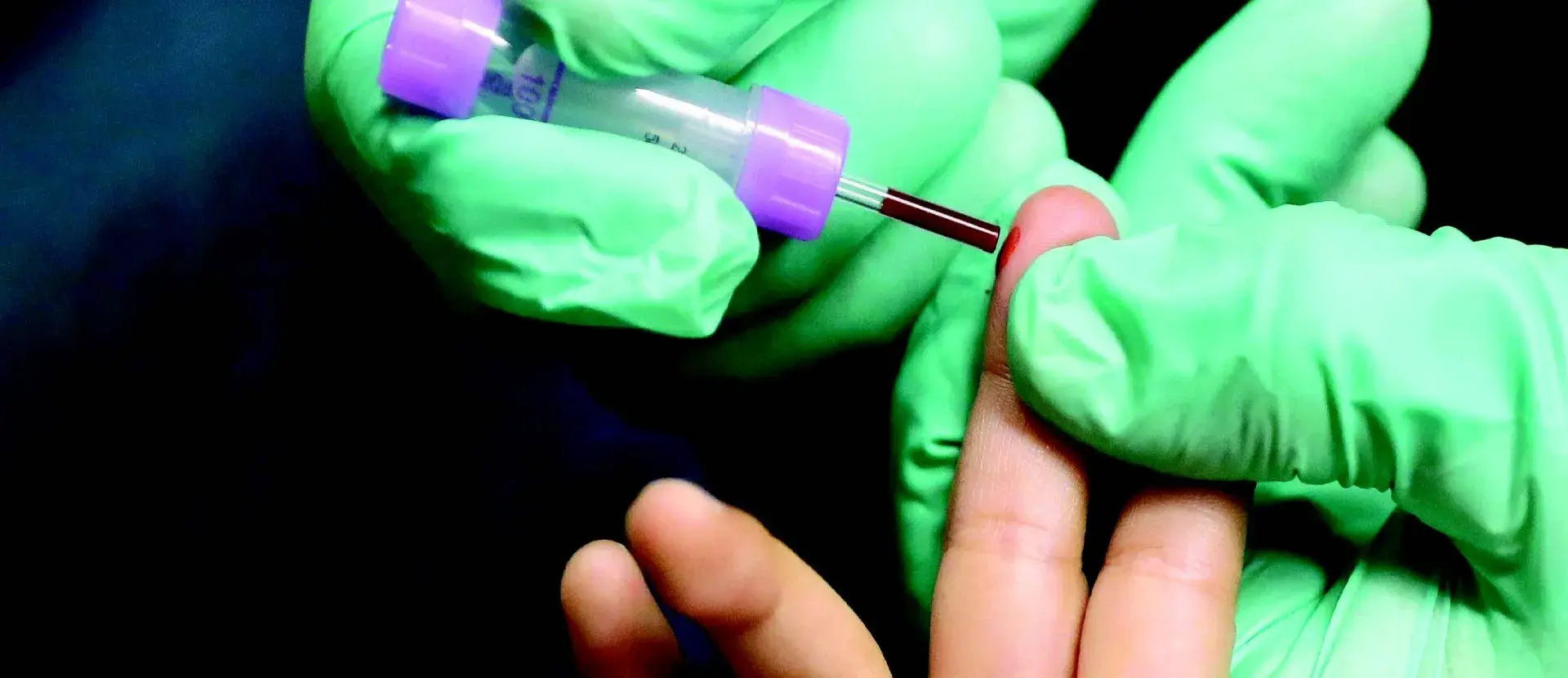 Hand with gloves drawing blood from a person's middle finger on their left hand